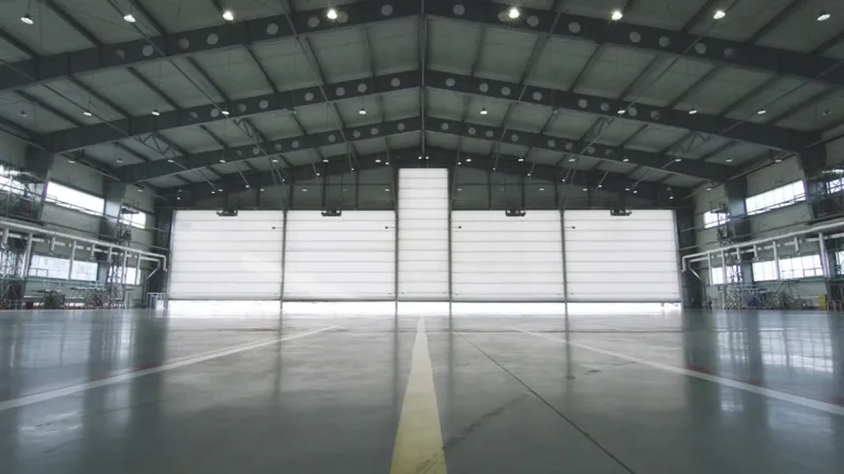 Roller shutter door and concrete floor inside factory building for industrial background. Airplane in front of half opened door to hangar. The open door of the hangar.